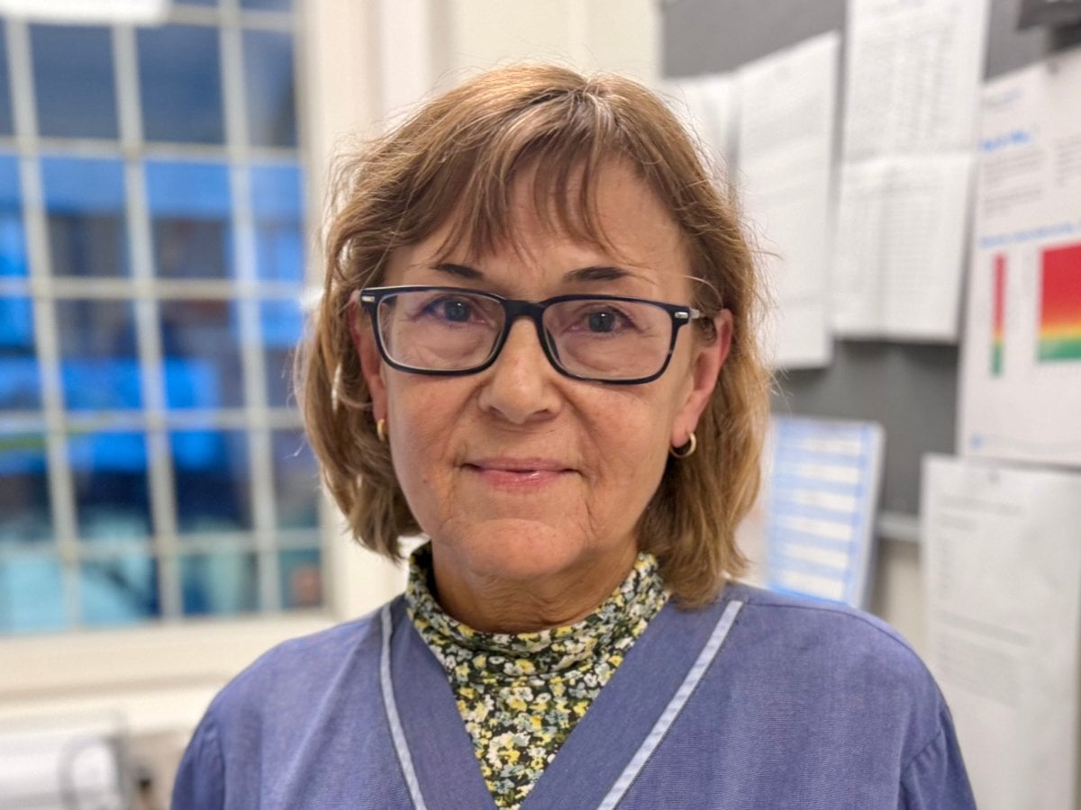 En kvinna i blå sjuksköterskekostym står i sitt kontor.