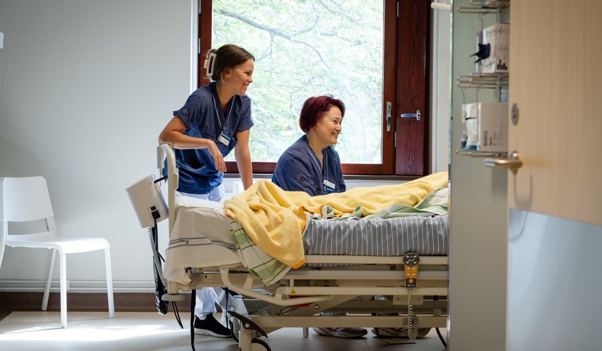 En kvinna står bredvid en kvinna i en sjukhussäng.
