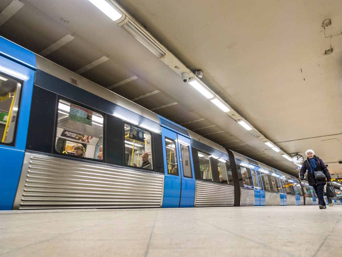 Tunnelbanetåg avgår från Slussens tunnelbanan. En äldre kvinna syns gå längs med perrongen.