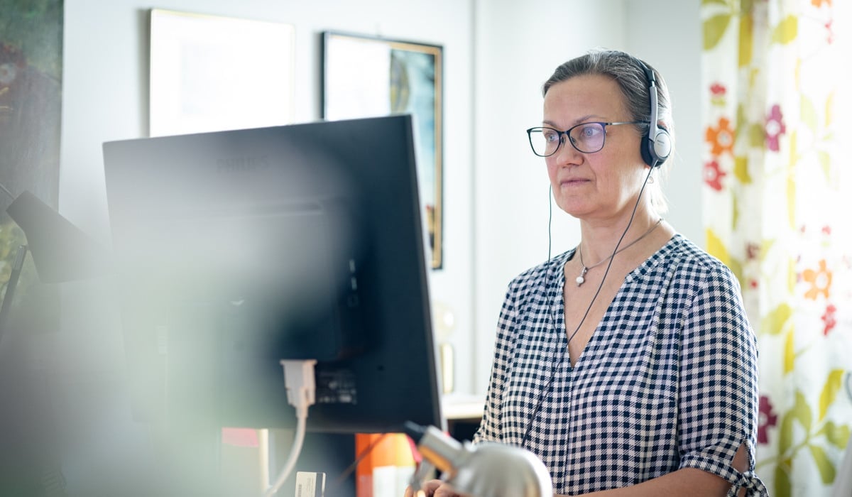 En kvinna med hörlurar på sig och använder en dator.