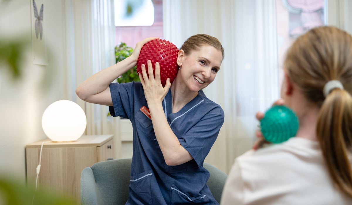 En kvinna sitter i en soffa och håller i en röd boll.