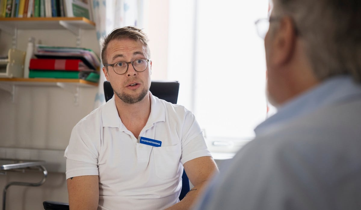 En man sitter i en stol och pratar med en annan man.