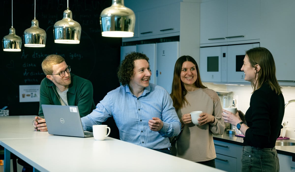 Kollegor står vid ett bord och pratar och dricker kaffe.