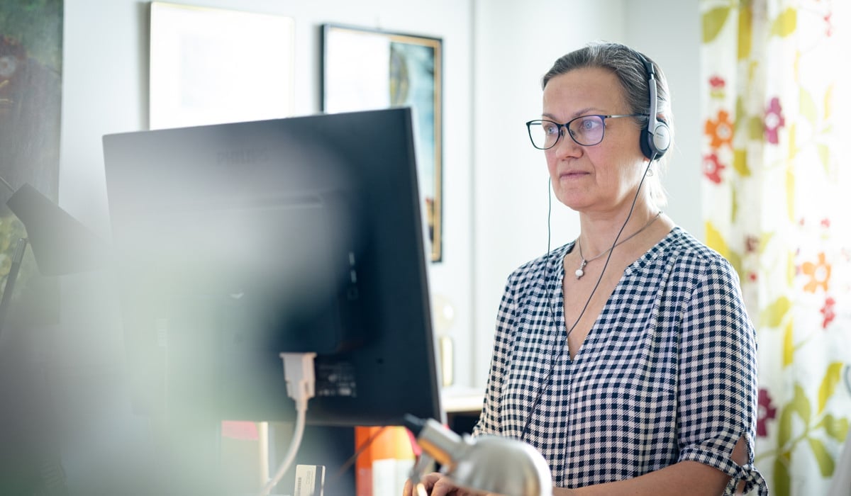 En kvinna med hörlurar på sig och använder en dator.