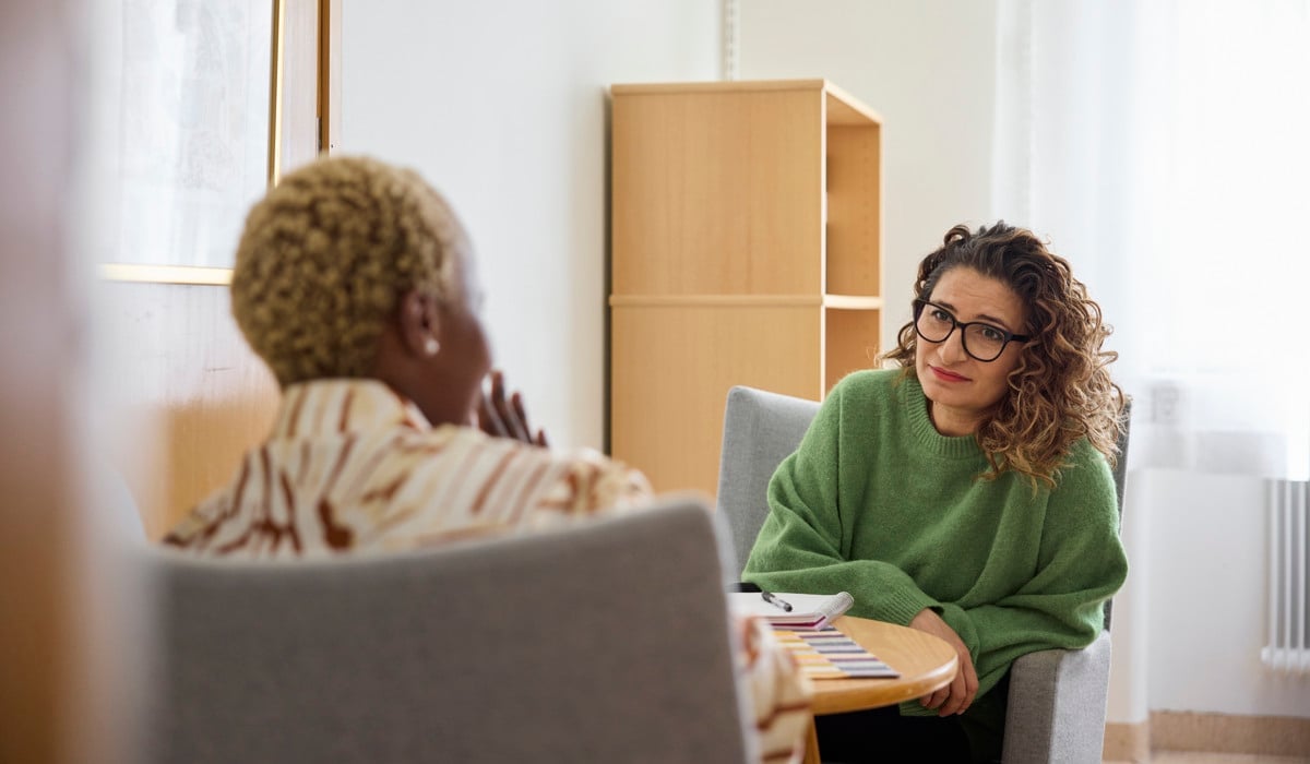Två kvinnor sitter i fåtöljer vid bord och samtalar