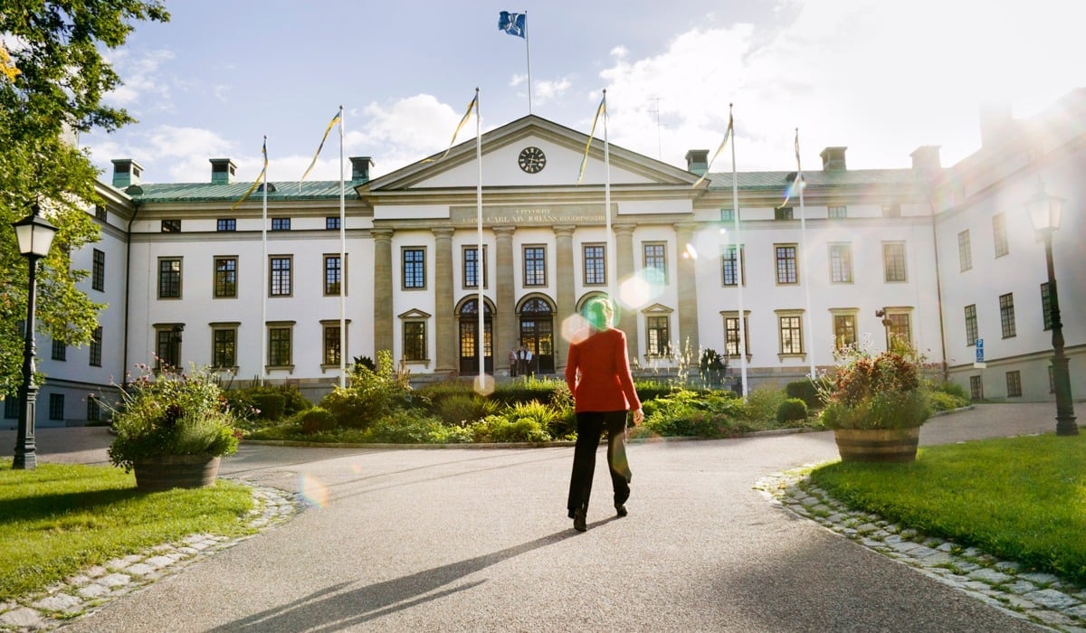Person går mot landstingshuset och solen skiner över parken