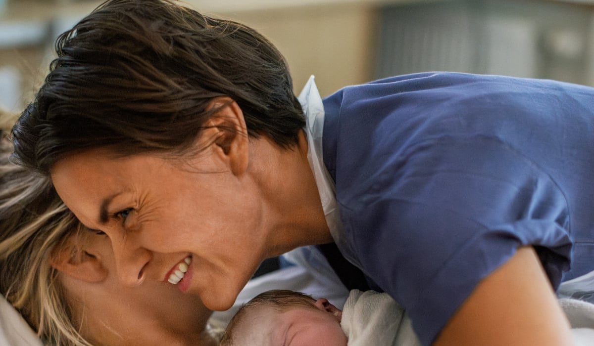 En barnmorska kramar om en kvinna som precis har fått sitt barn.