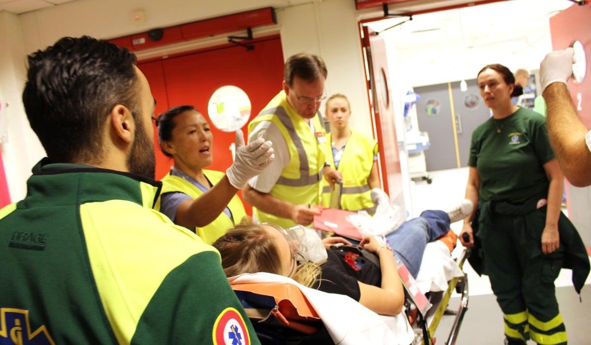 Vårdmedarbetare övar på katastrofmedicin. En kvinna ligger på en bår och runt henne flertalet läkare, sjuksköterskor och annan vårdpersonal i varselvästar. 