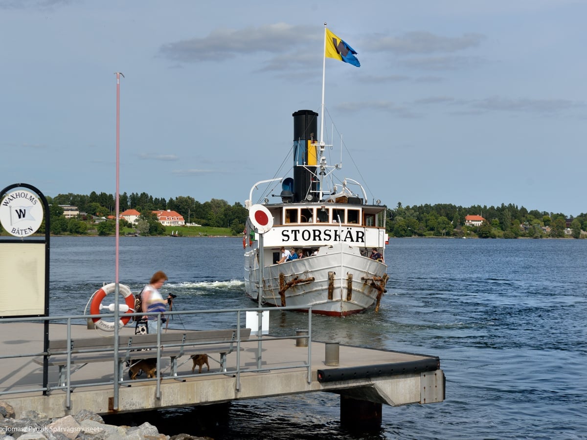 Passagerare står på brygga och en skärgårdsbåt är på väga att lägga till.