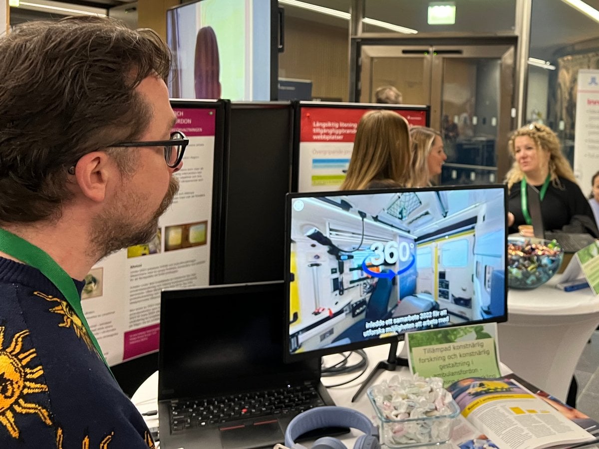 Film från insidan av ambulans på en skärm i kulturförvaltningens monter. Till vänster i bild står Finbar och tittar på skrämen,