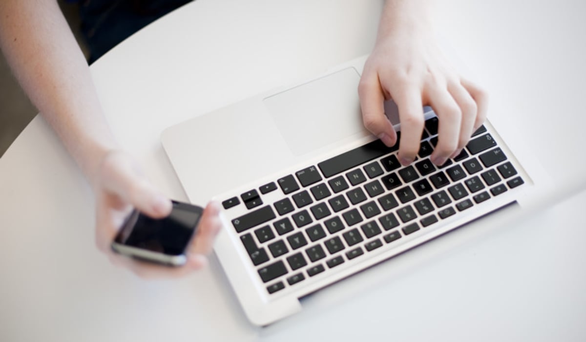 Foto på händer som skriver på ett tangentbord och håller i en telefon.
