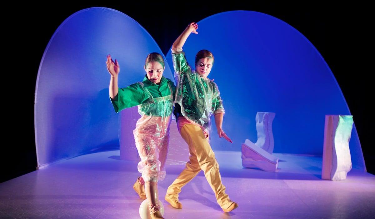 Två personer i färgglada kläder rör sig på en scen.