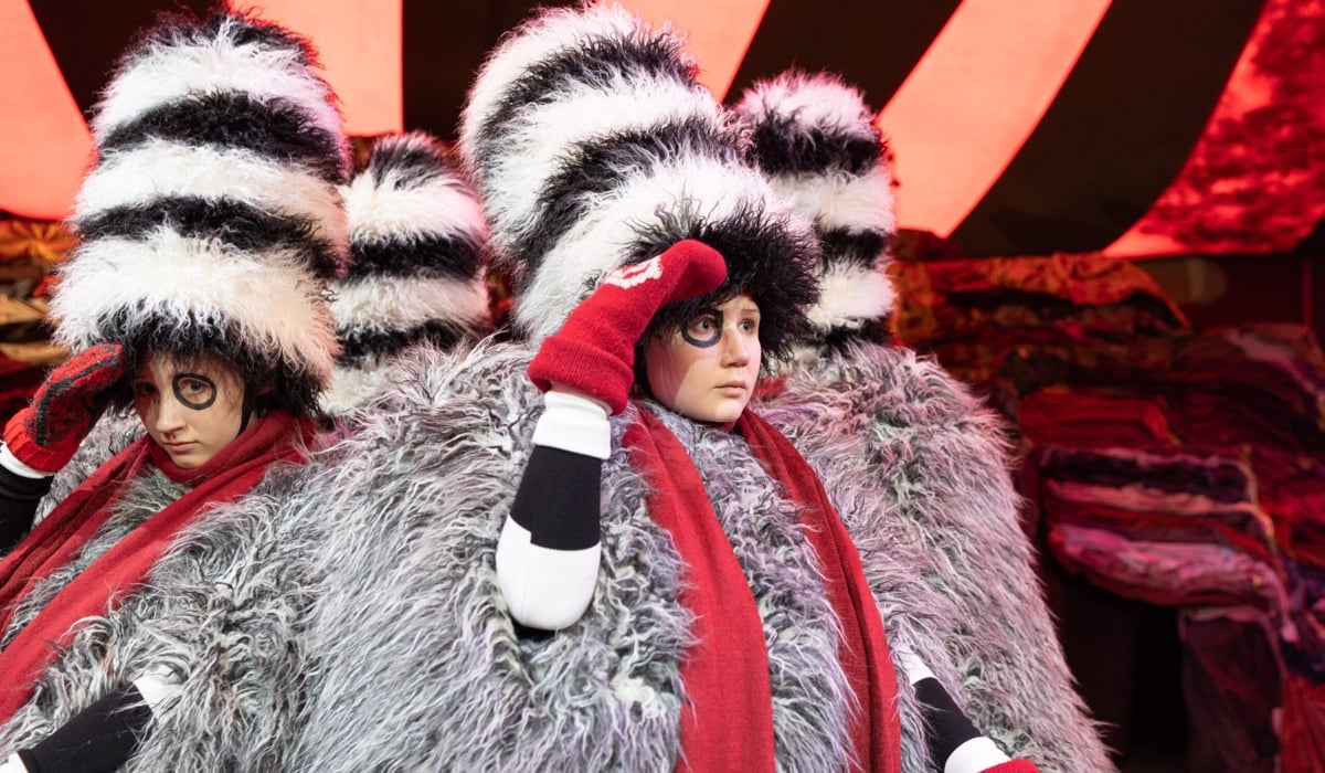 Barnskådespelare på scen i lurviga svartvita dräkter med röda mössor och röda halsdukar