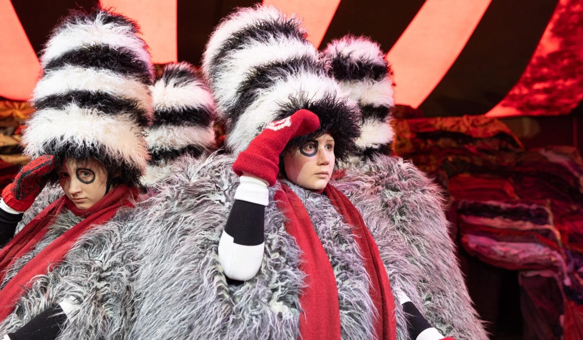 Barnskådespelare på scen i lurviga svartvita dräkter med röda mössor och röda halsdukar