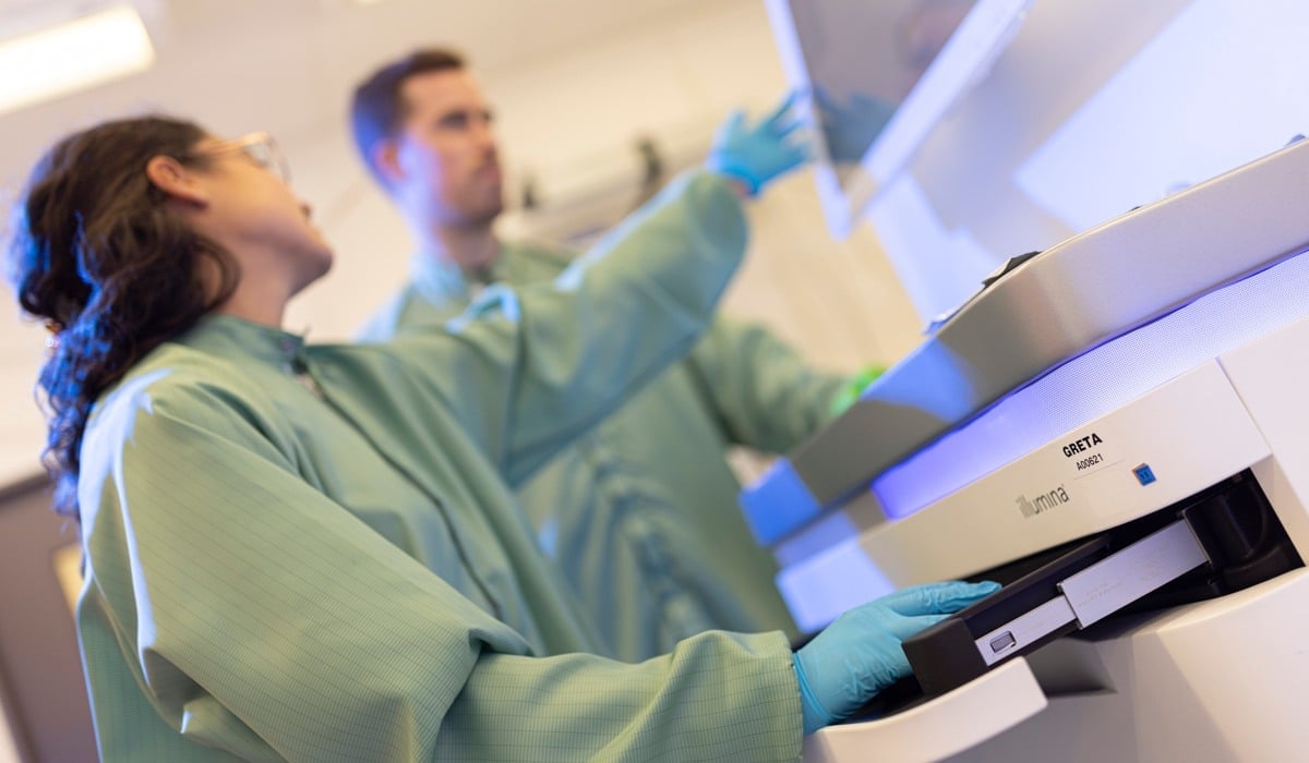 Två forskare i gröna rockar som står vid en maskin i ett laboratorium