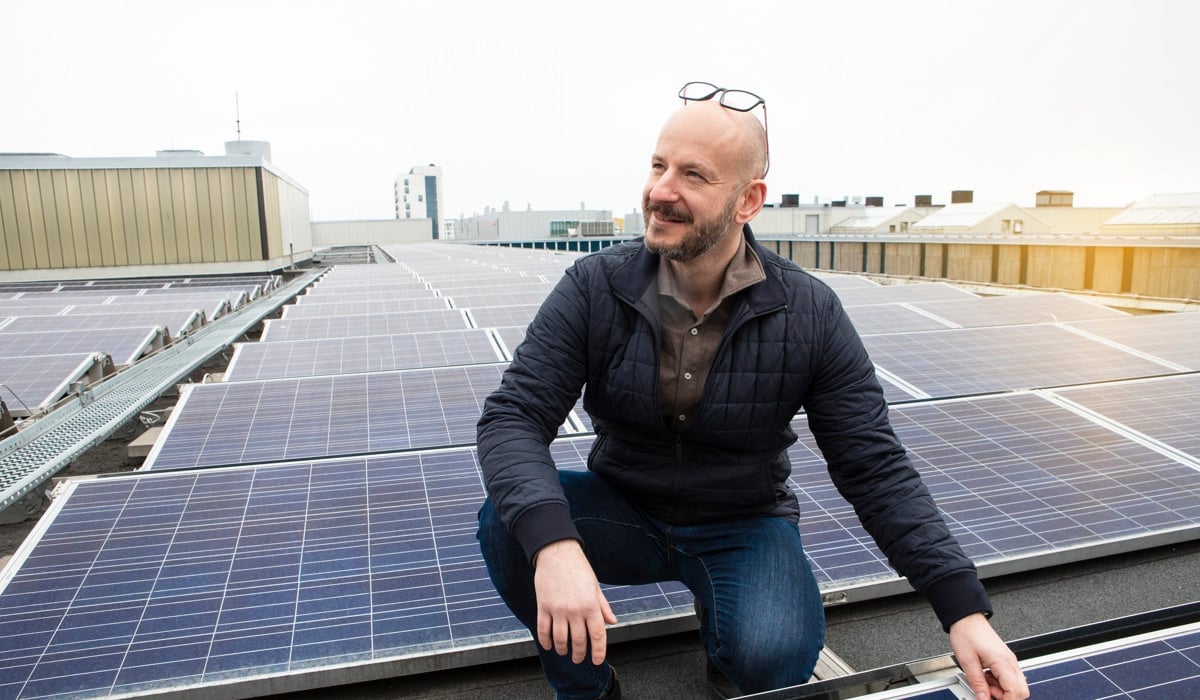 Foto på en man som är upp på ett tak där det finns solceller.