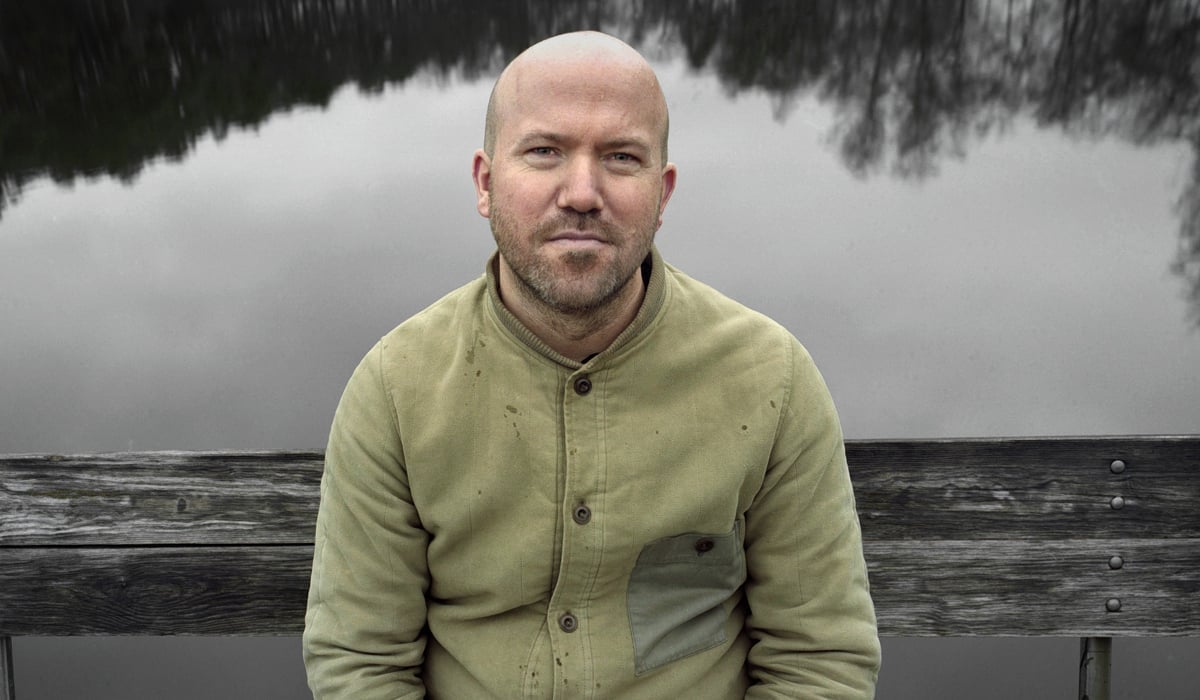 En skallig man sitter på en bänk intill en sjö.