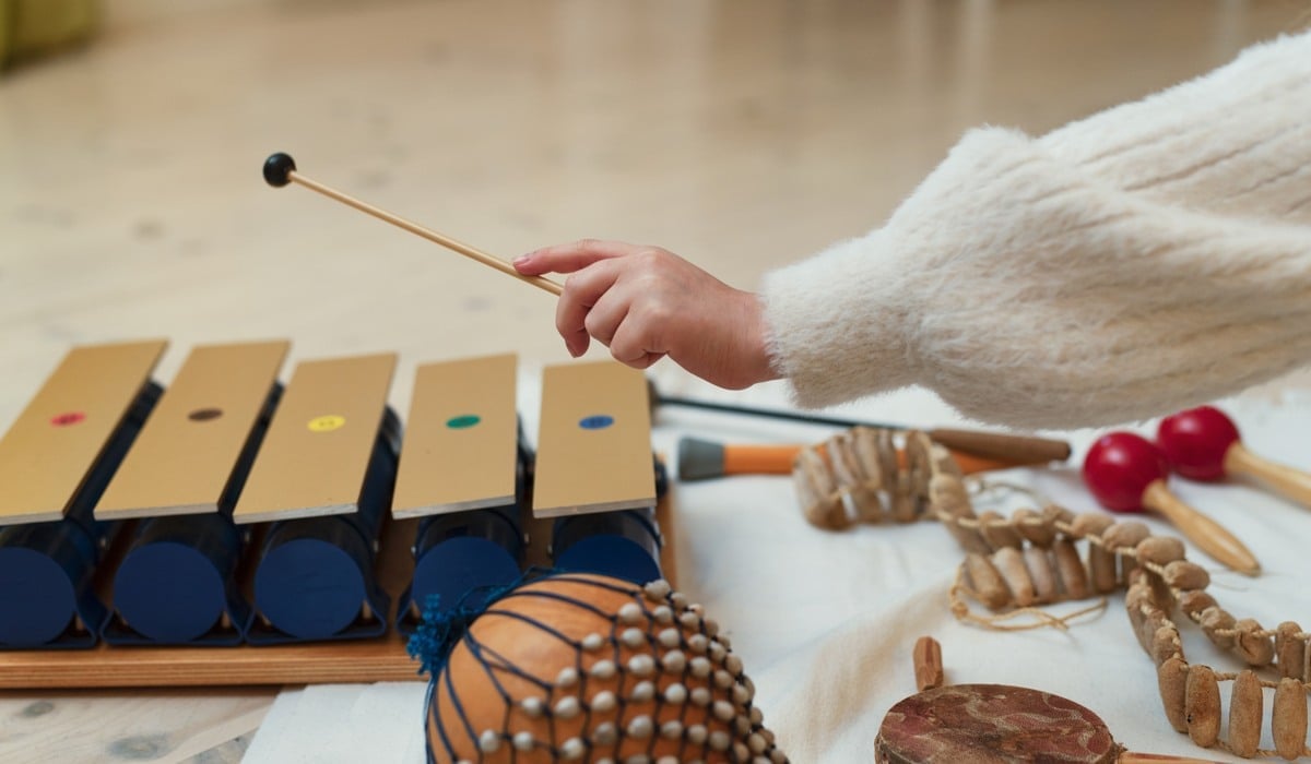 Foto på ett barn sitter på golvet och spelar på en xylofon. Det ligger andra instrument framför barnet.