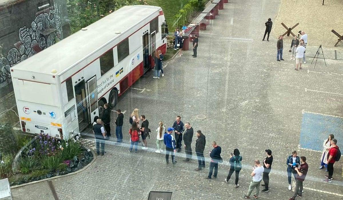 Foto taget uppifrån över ett torg. En blodbuss står parkerad på torget och det är flera personer som köar för att ge blod.