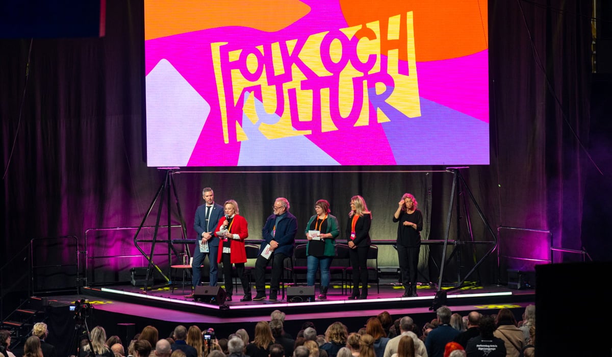 Ett publikhav framför en scen med en panel och en skärm där det står Folk och kultur