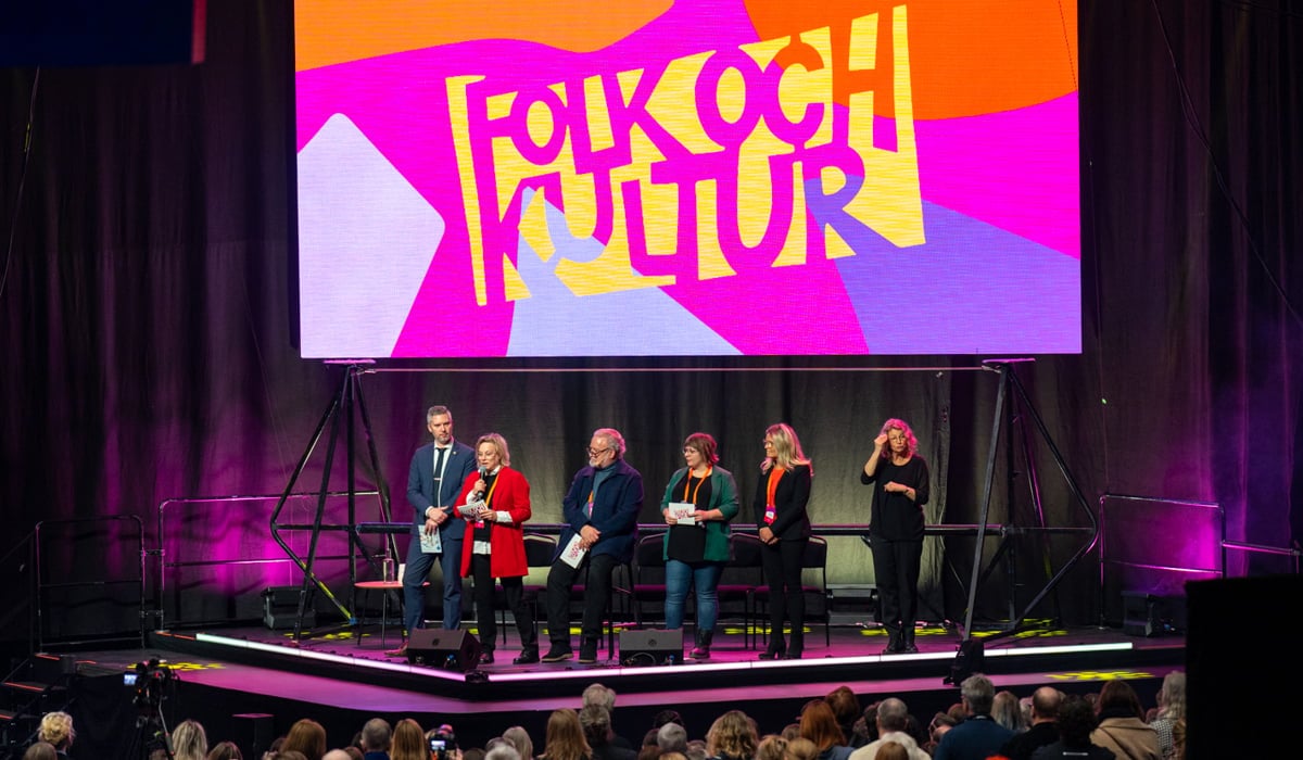 Ett publikhav framför en scen med en panel och en skärm där det står Folk och kultur