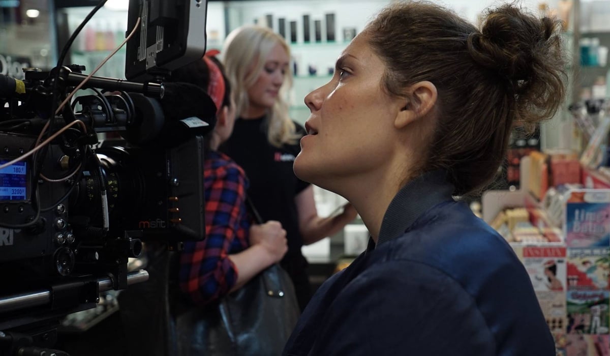 En kvinna med en filmkamera i en affär. Två unga kvinnor står och pratar.