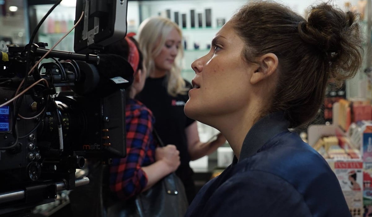 En kvinna med en filmkamera i en affär. Två unga kvinnor står och pratar.