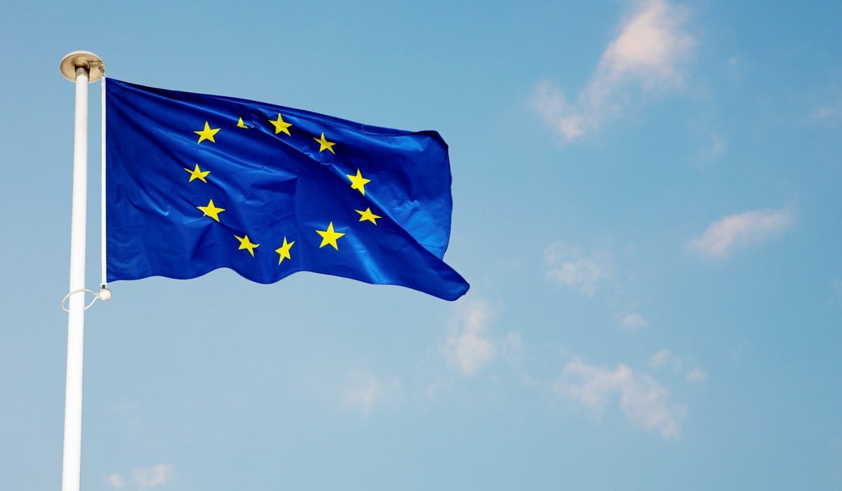 Bild på en blå EU-flagga som vajrar på en vit flaggstång med blå himmel i bakgrunden